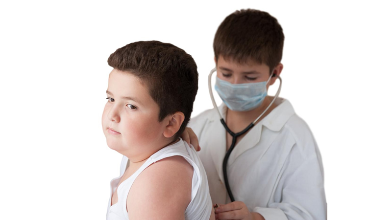 boy sitting with another masked boy behind with stethoscope on back