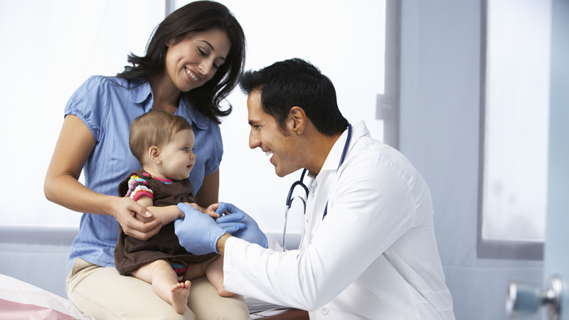 smiling doctor talking to baby on moms lap