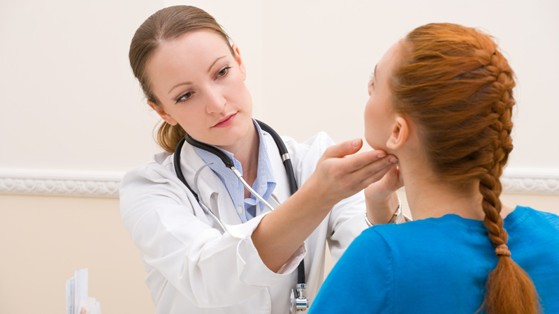 woman in white lab coat with stethoscope examining a womans neck glands