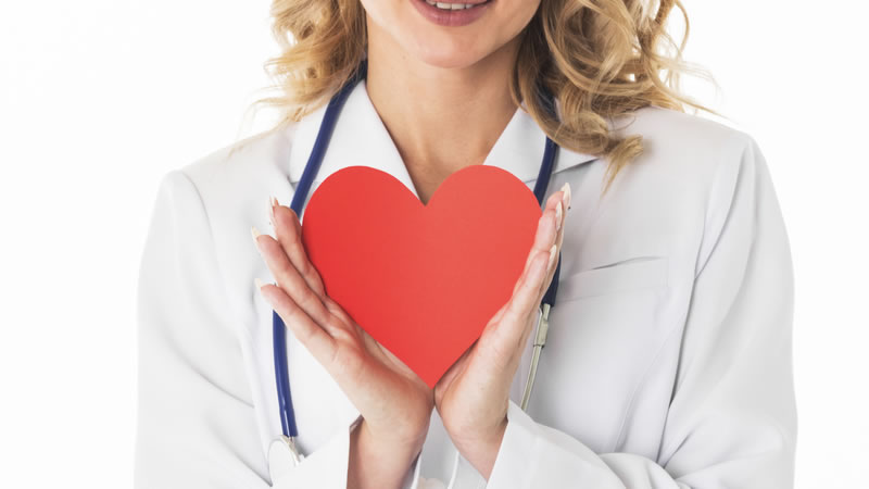 woman in white lab coat with stethoscope holding red heart
