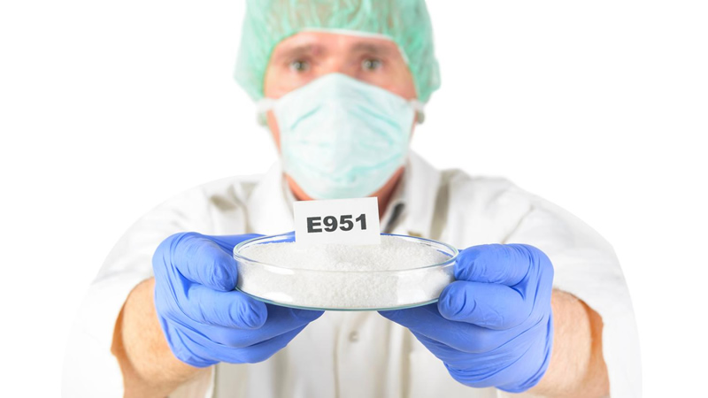 lab tech masked and gloved holding out poison Aspartame E951