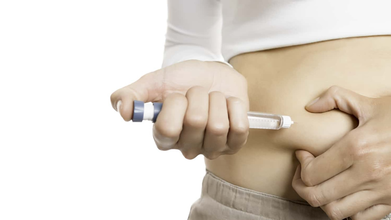 close up of hypodermic needle being inserted by a woman into her abdomen
