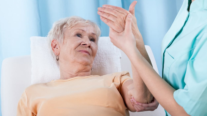 older woman reclining, person beside holding her arm as if to test range of motion