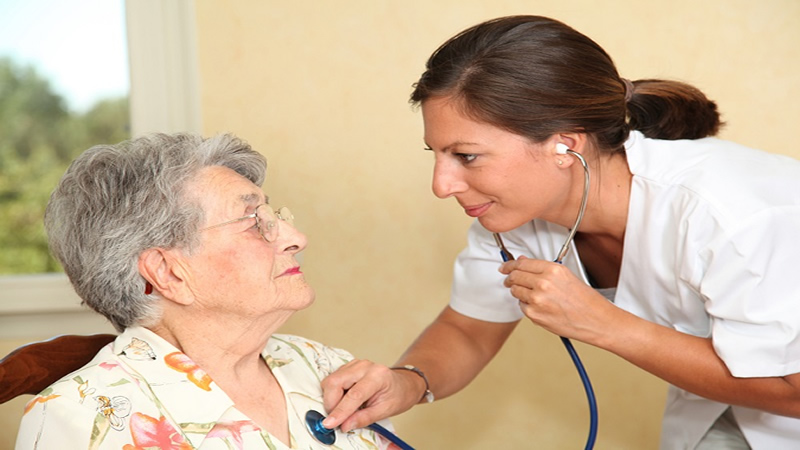 woman in white lab coat with stethoscope listening to older womans heart