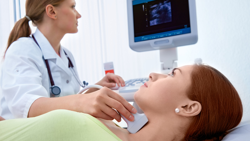 woman in white lab coat with stethoscope doing ultrasound on patients neck, thyroid gland