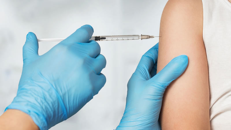 gloved hands giving needle to upper arm