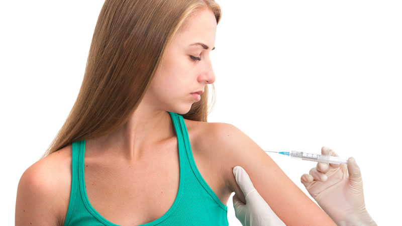 gloved hands giving needle to young womans upper arm