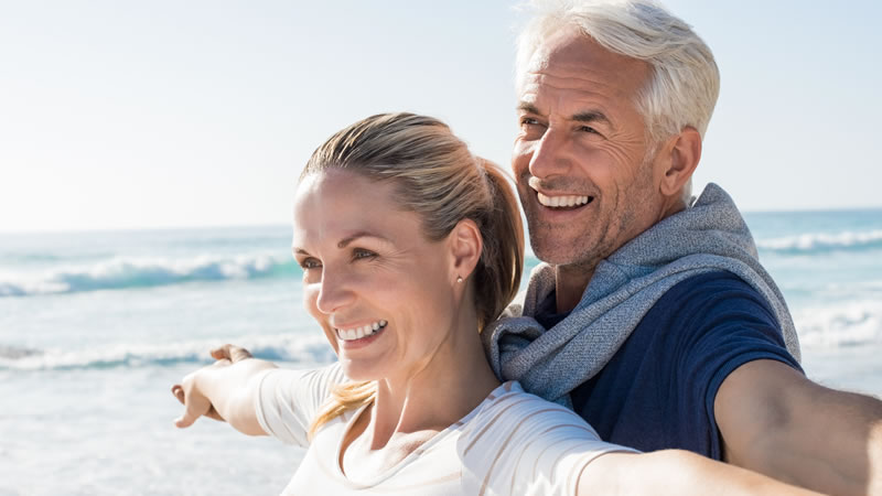 mature happy couple on beach with arms held outstretched