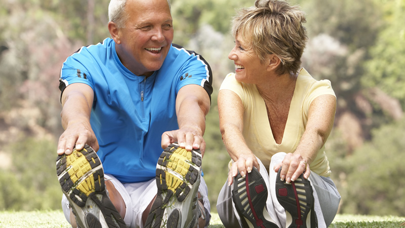 older healty smiling couple sitting and touching their toes, stretching hamstrings