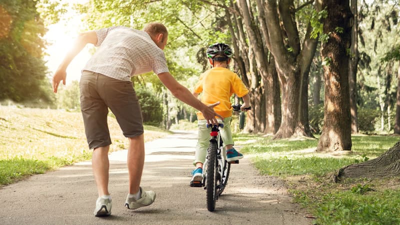dad teaching son to ride a two-wheeler bike, holding seat for balance