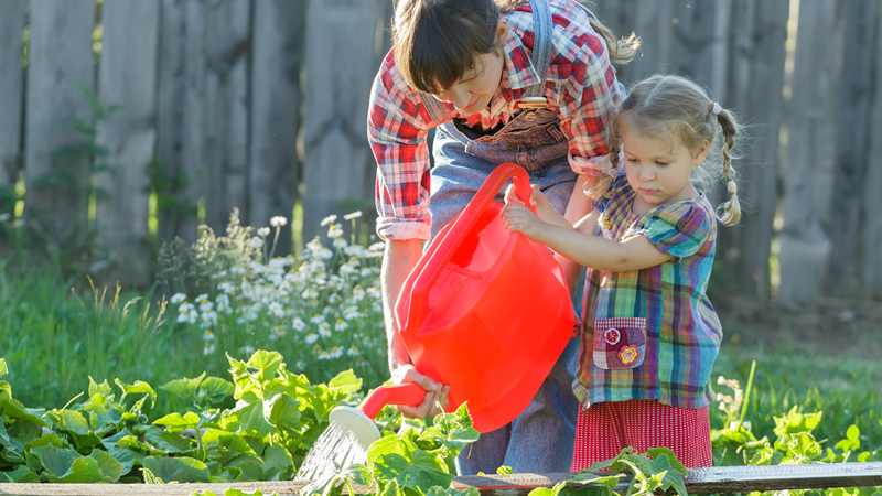 young mom and daughter watering garden plants