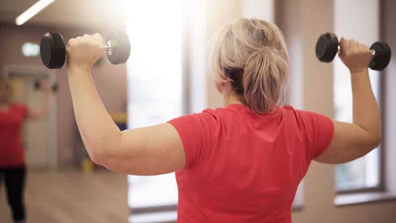 woman lifting weights above, watching herself in mirror