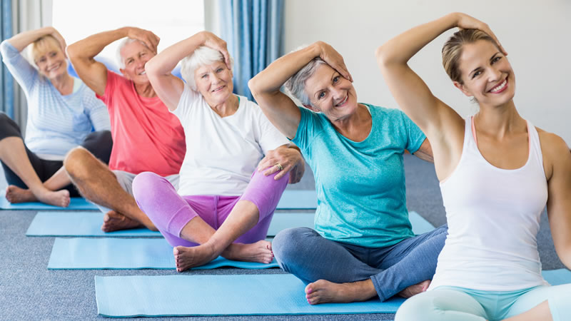 women lined up stretching, sitting on yoga mats