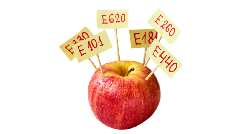 red apple with little stick signs showing GMO letters and numbers