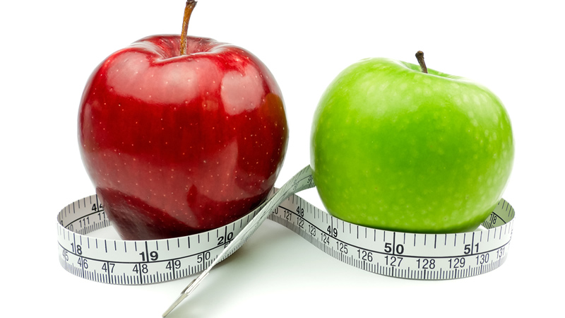 red apple and green apple surrounded by measuring tape