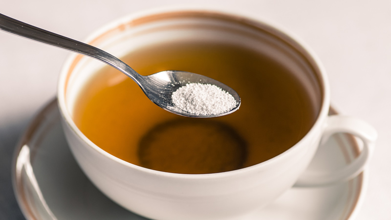 aspartame on spoon above mug of tea