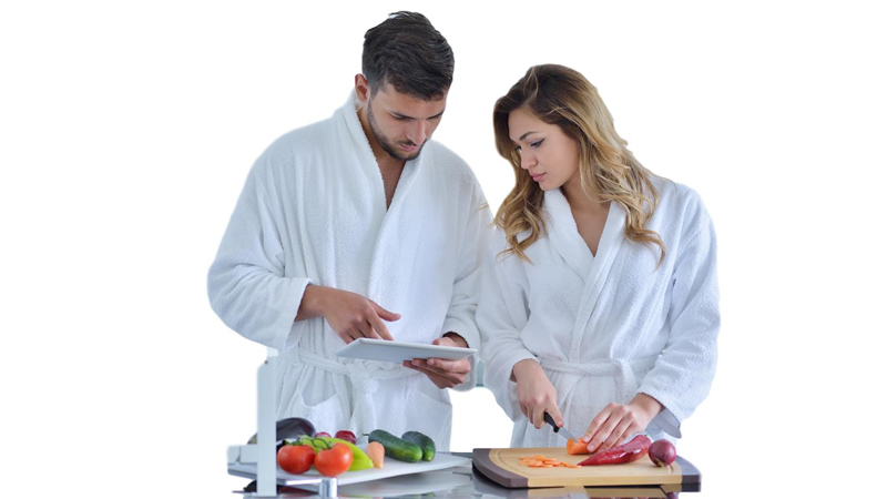 young couple in white robes preparing food and looking at tablet