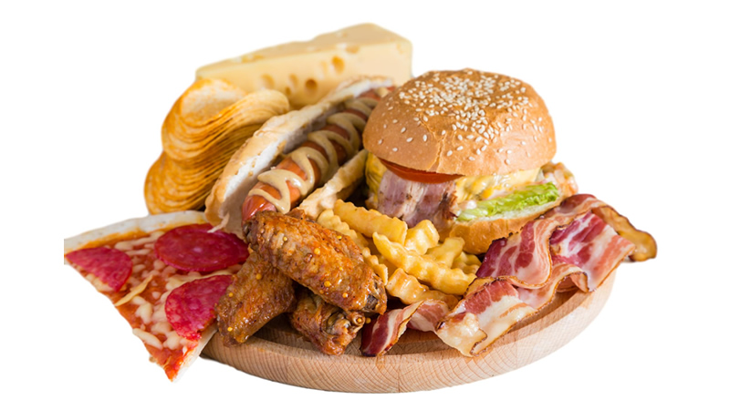 wood tray with high fat foods, pizza, chicken wings, potatoe chips, bacon, fries, burger and hot dog