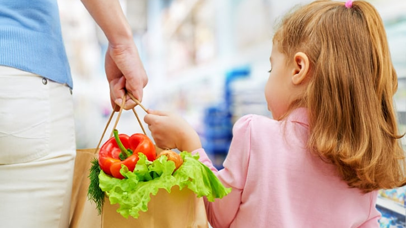 grocery bag full of vegetables being held between mother and daughter
