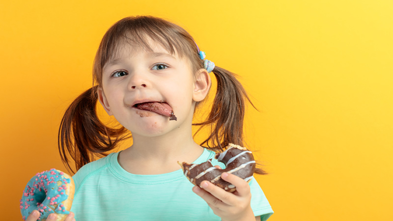 young girl holding 2 donuts licking her lips