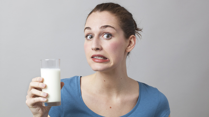 woman holding glass of milk grimacing as if its not good