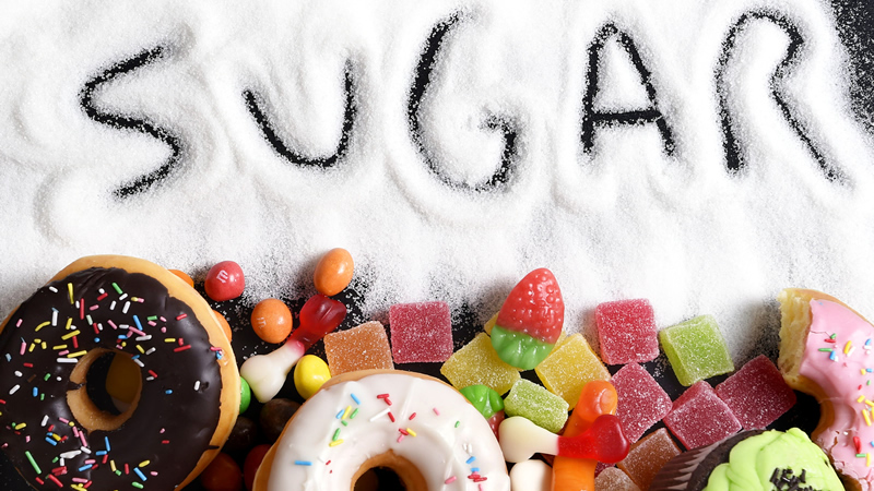 word sugar written in pile of white sugar with donuts and candy