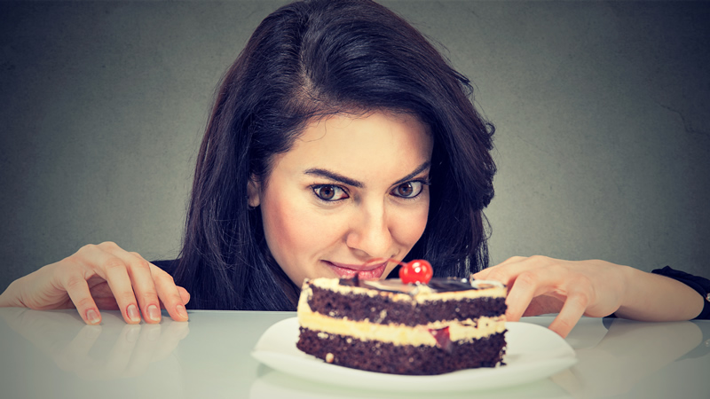 close up of womans face looking longingly at piece of chocolate cake