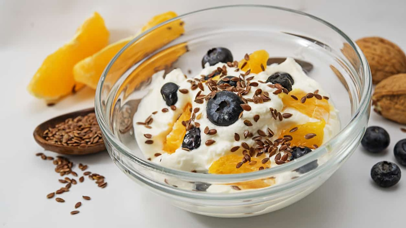 clear glass bowl of yogurt, orange slices, blueberries and flax seeds