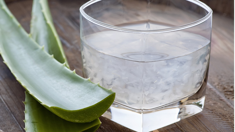 clear glass Aloe Vera Juice with 2 cut leaves beside
