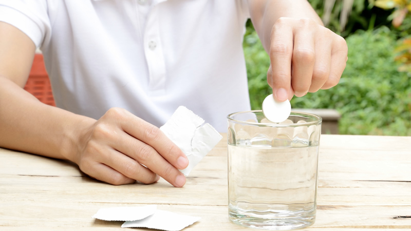 hands putting effervescent tablet into glass of water