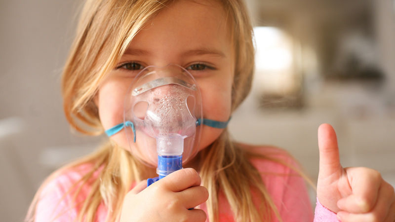 young girl smiling and holding oxygen or nebulizer on face with one thumb up
