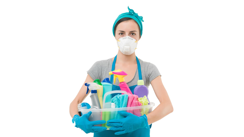 masked and gloved woman with armful of toxic cleaning products