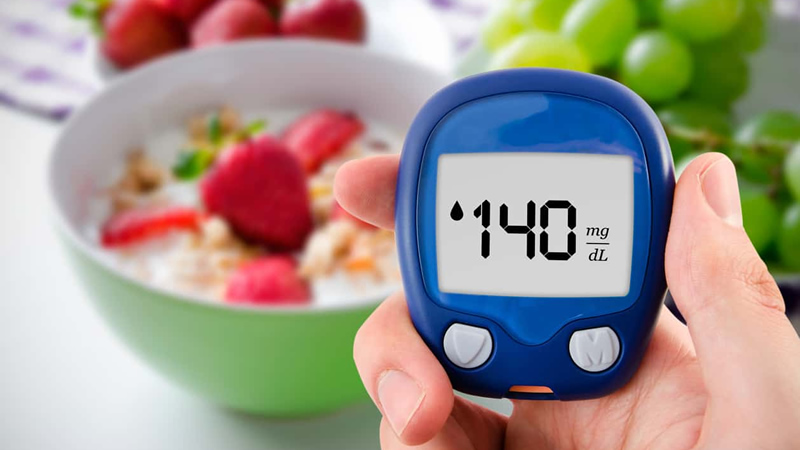 diabetes blood glucose monitor reading 140mg/dL with bowl of fruit behind