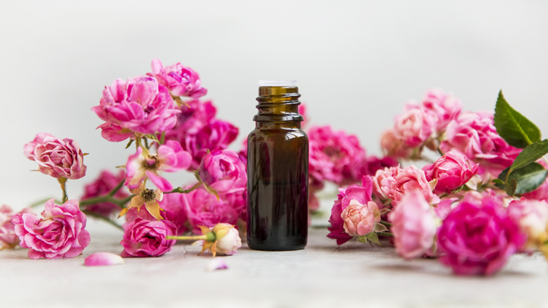brown dropper bottle of essential oil surrounded by rose blooms