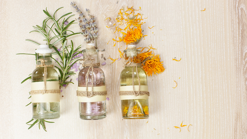 3 clear bottles essential oils with scattered herbs
