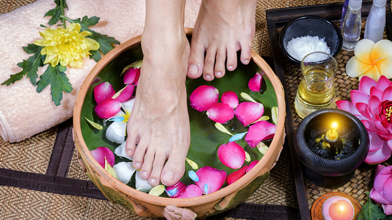 pretty womans feet in wooden foothbath with bubbles and pink flower petals