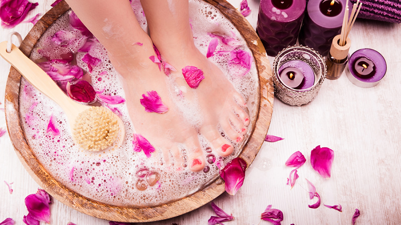 pretty womans feet in wooden foothbath with bubbles and scattered pink flower petals