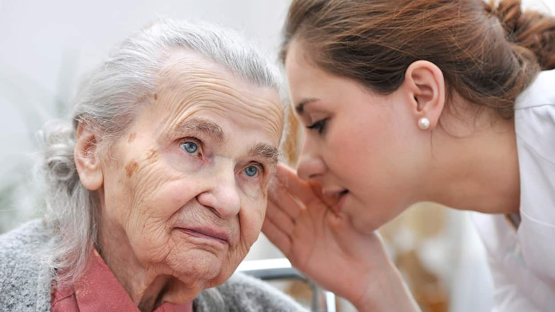 older white haired woman listening to younger woman whispering into her ear