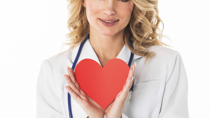 smiling woman in white lab coat with stethoscope holding red heart