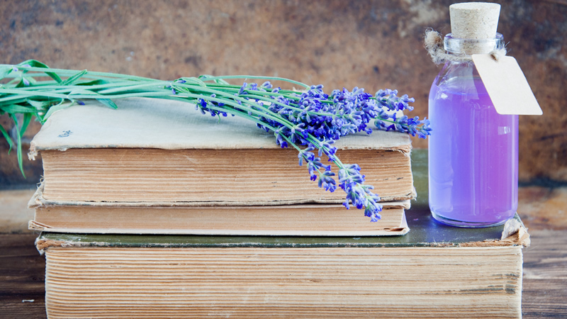 sprig of lavender and bottle of essential oil on stack of hardcover books