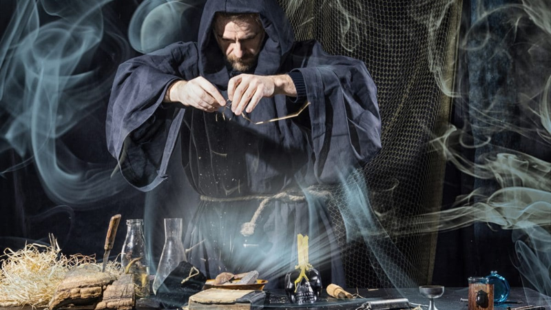 man in black cloak with hands over table as if performing magic