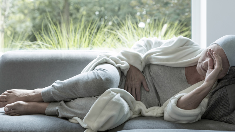 older woman with scarf on head as if suffering with cancer, lying on couch