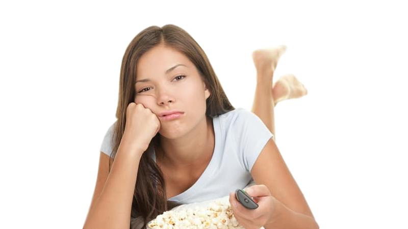 young teen with sad face resting on fist behind bowl of popcorn with TV remote control
