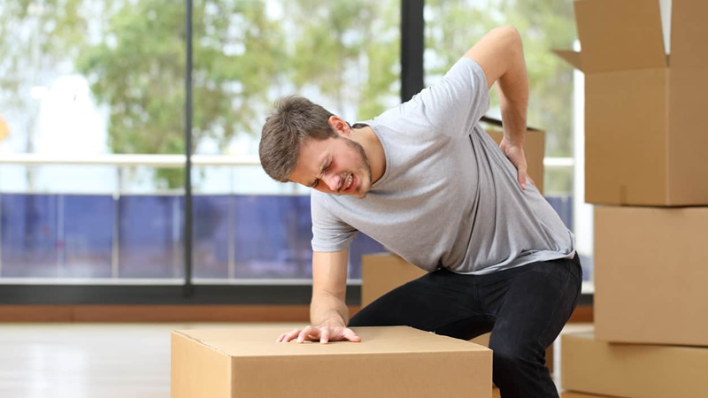 young man with moving boxes, hand on back grimacing in pain