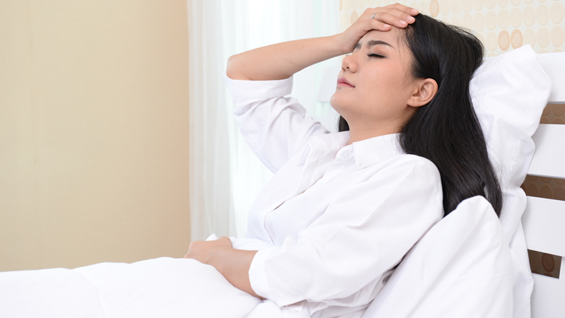 woman reclining with hand on her forehead as if in pain