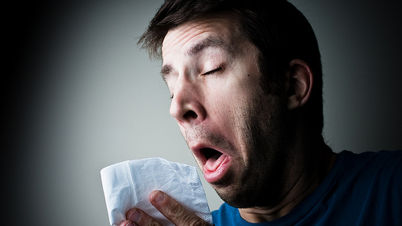 man with face contorted about to sneeze into tissue