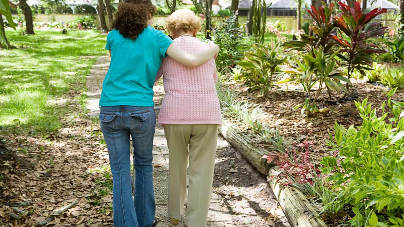 back view young woman helping older woman walk in park