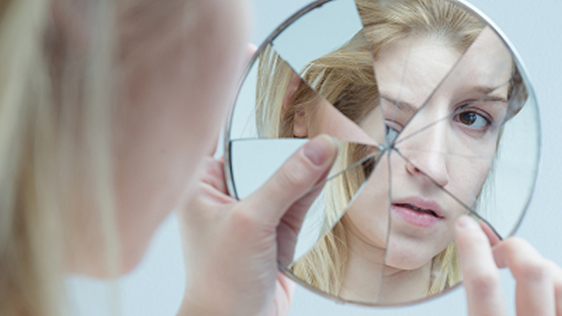woman looking at face in a cracked mirror