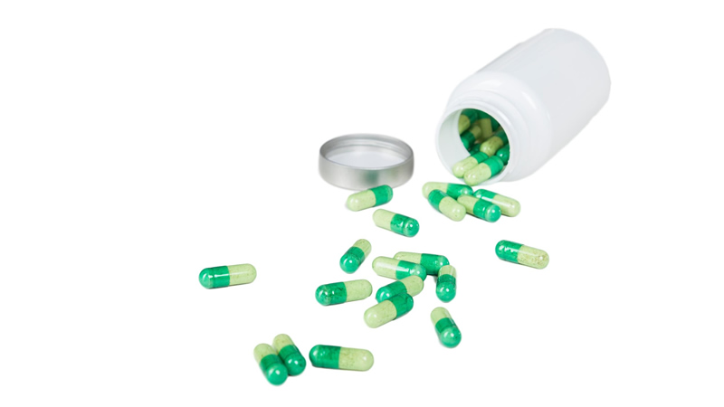 green capsules spilling out of white bottle
