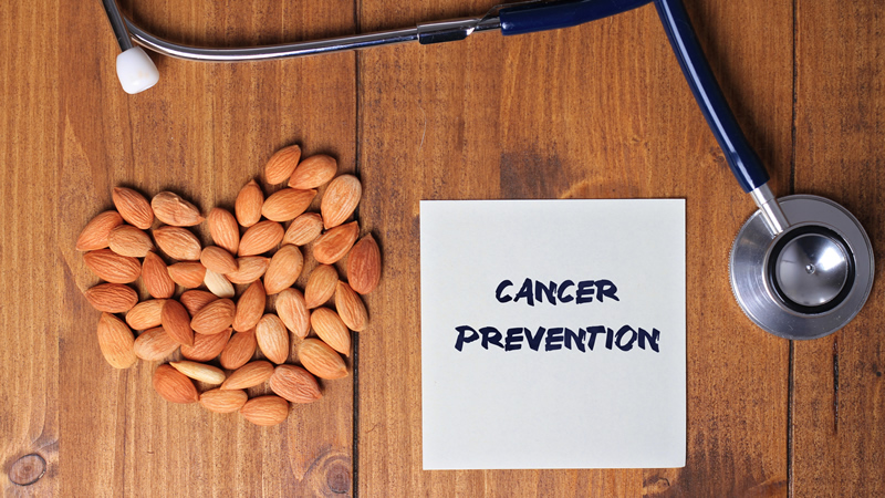 top view of the words Cancer Prevention on paper beside pile of almonds in heart shape and stethoscope